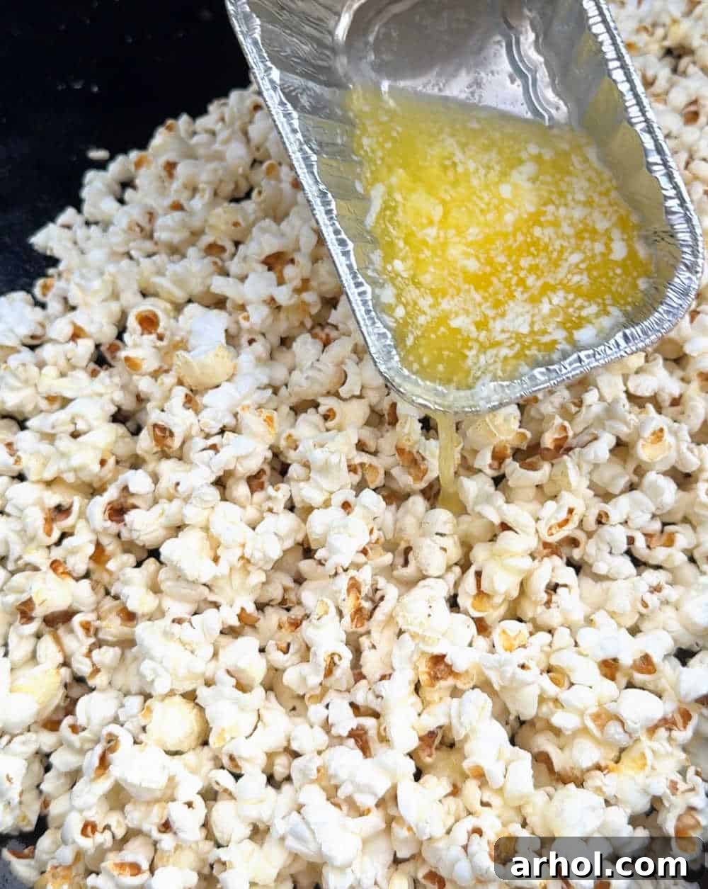 pouring melted butter over popped corn on Blackstone grill.