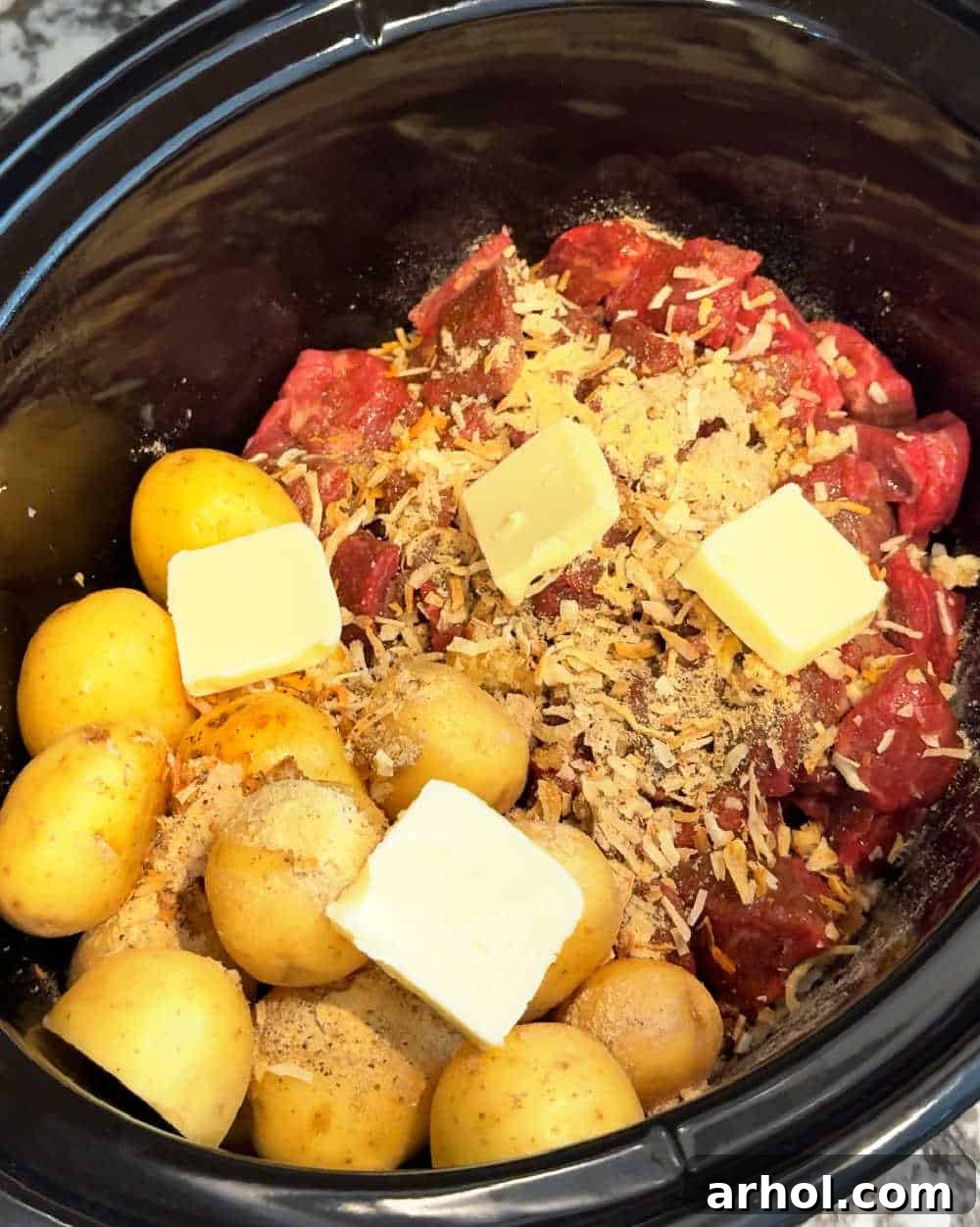 Pats of butter placed on top of meat and potatoes in the slow cooker.