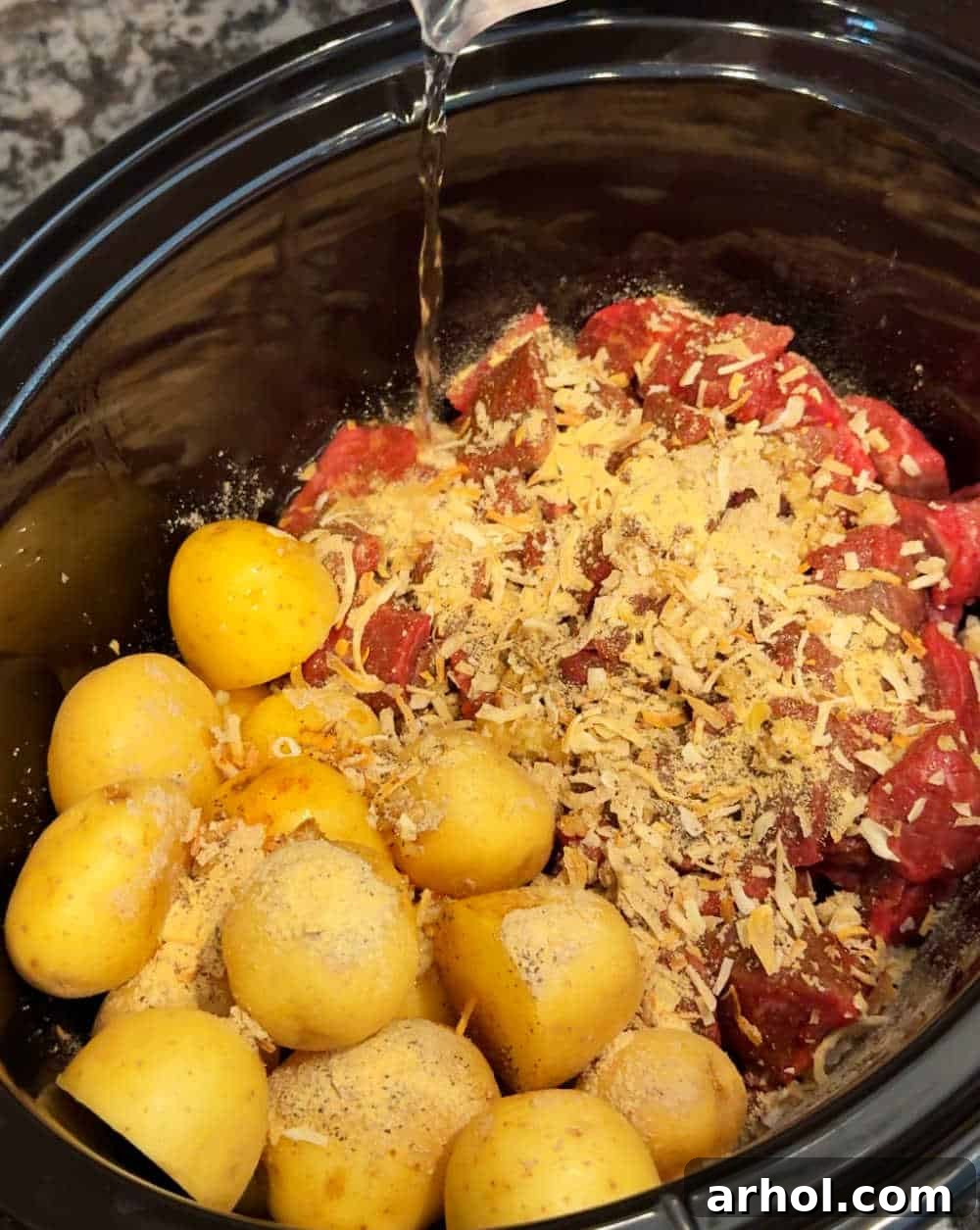 Pouring water into the slow cooker with beef, potatoes, and seasonings.