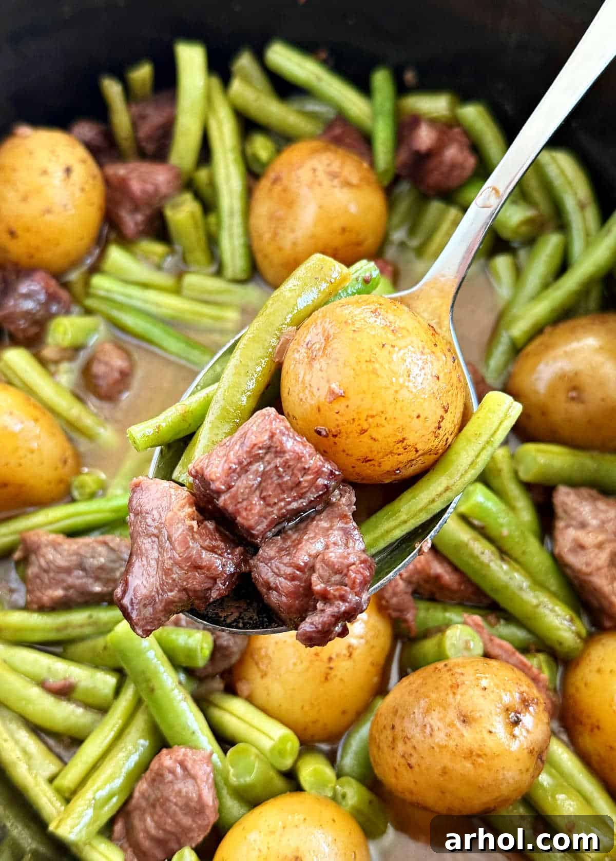 Serving of garlic butter beef bites, potatoes, and green beans on a spoon, showcasing tender meat and vegetables.