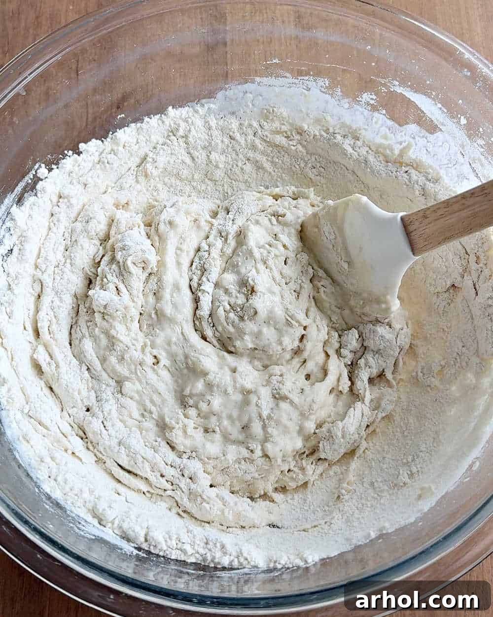 Mixing bread flour into the sourdough starter and water mixture with a spatula to form the initial dough.