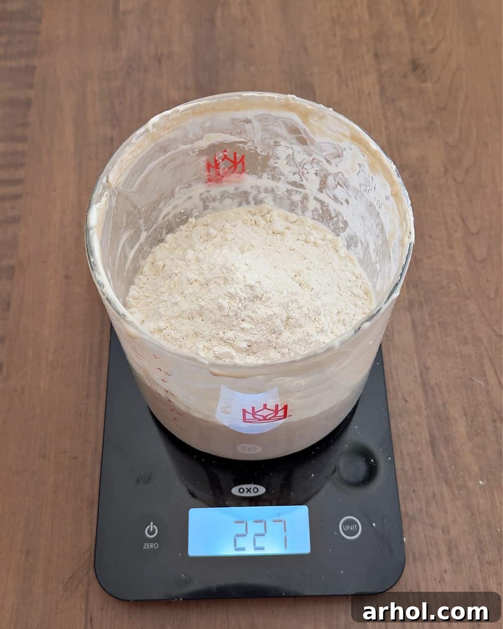 Adding flour to the starter and water mixture in the crock on a scale.