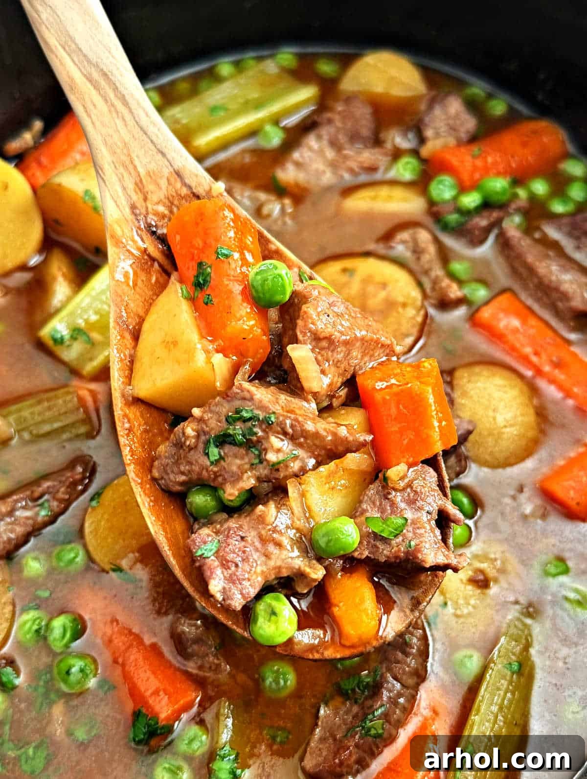 A serving spoon lifting a spoonful of slow cooker beef stew with onion soup mix, carrots, and potatoes, showcasing the tender ingredients.