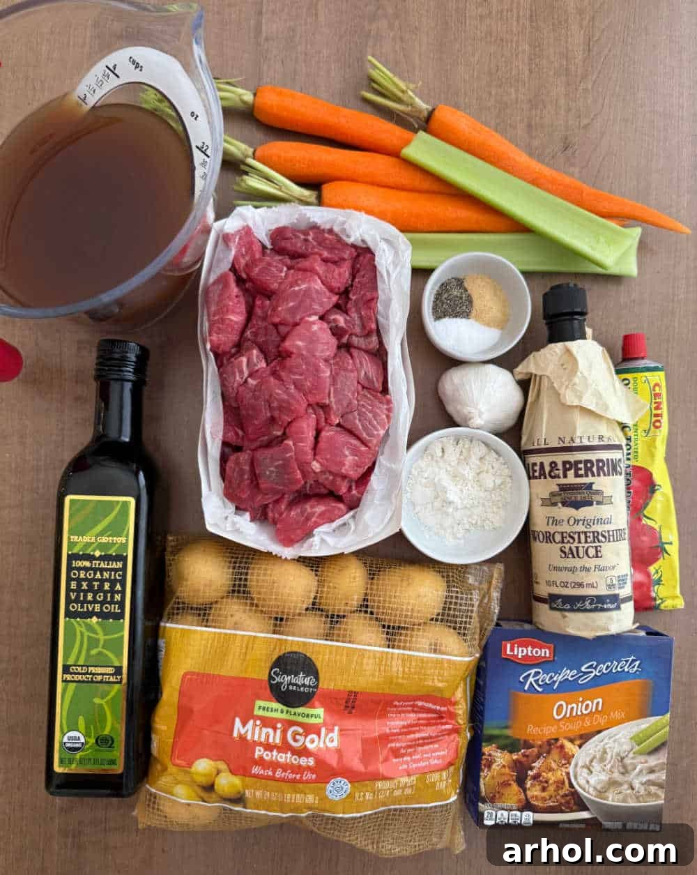 Raw beef stew meat, fresh carrots, baby potatoes, and celery laid out with other stew ingredients on a cutting board, ready for preparation.