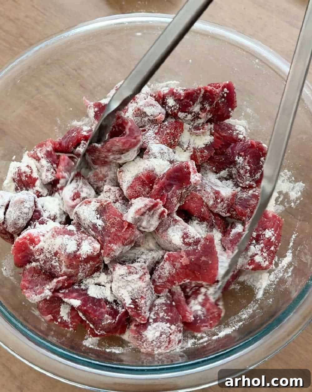 Tossing beef cubes with flour, salt, and pepper in a large mixing bowl to coat them evenly.