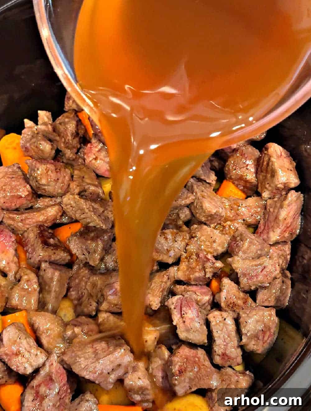 Pouring beef broth into the slow cooker, preparing the liquid base for the stew.