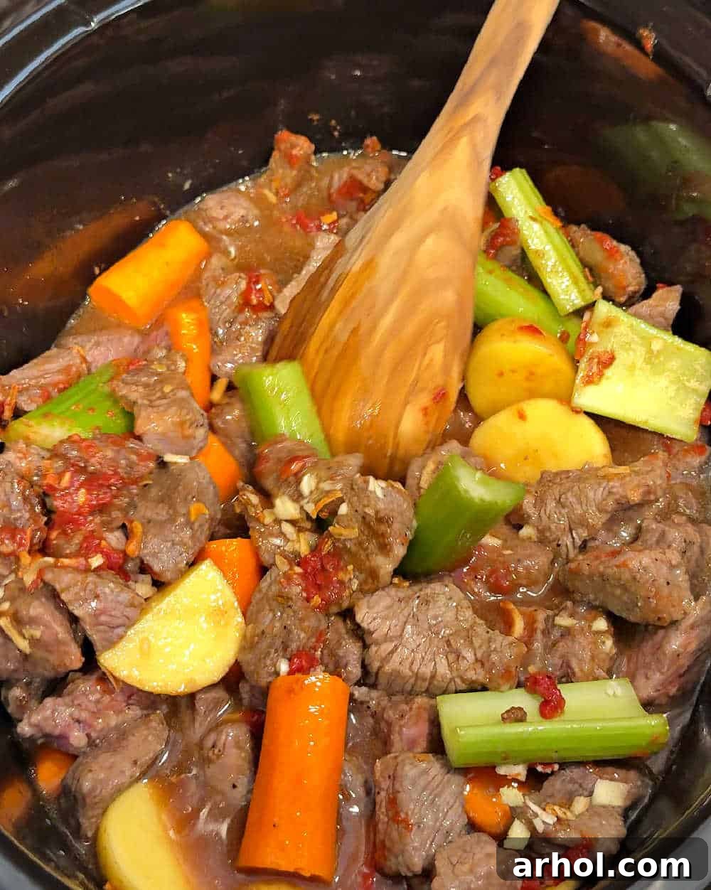 Stirring all the ingredients together in the crock pot: beef, vegetables, and sauce components.