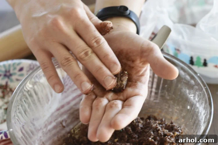 The sticky bourbon ball mixture being rolled by hand into small, uniform balls, a crucial step before coating them in sugar and sprinkles.