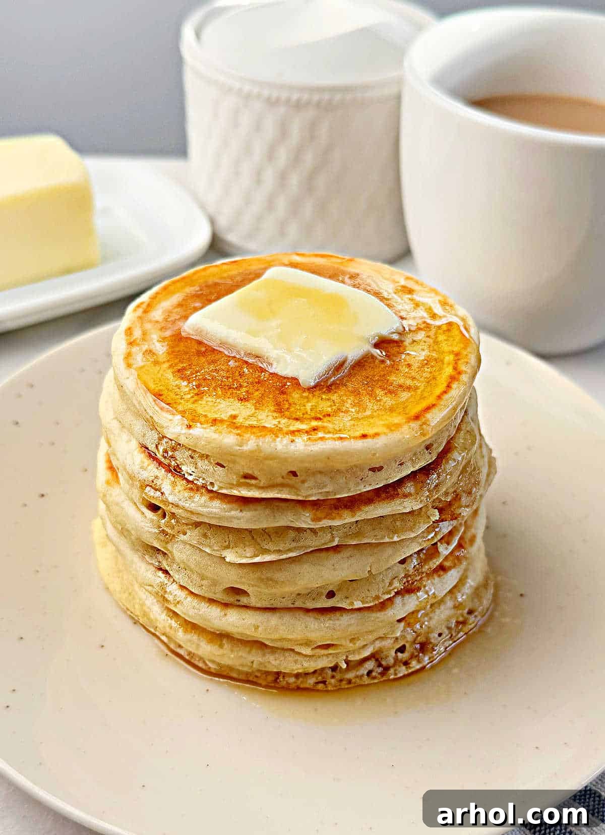 Stack of golden brown, fluffy sourdough pancakes with butter and syrup on a white plate, ready to be enjoyed for breakfast or brunch.