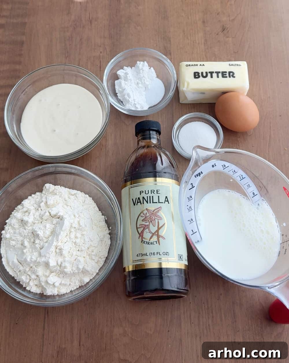 Key ingredients for sourdough discard pancakes laid out: flour, baking powder, sea salt, sugar, melted butter, vanilla extract, sourdough discard, milk, and an egg.