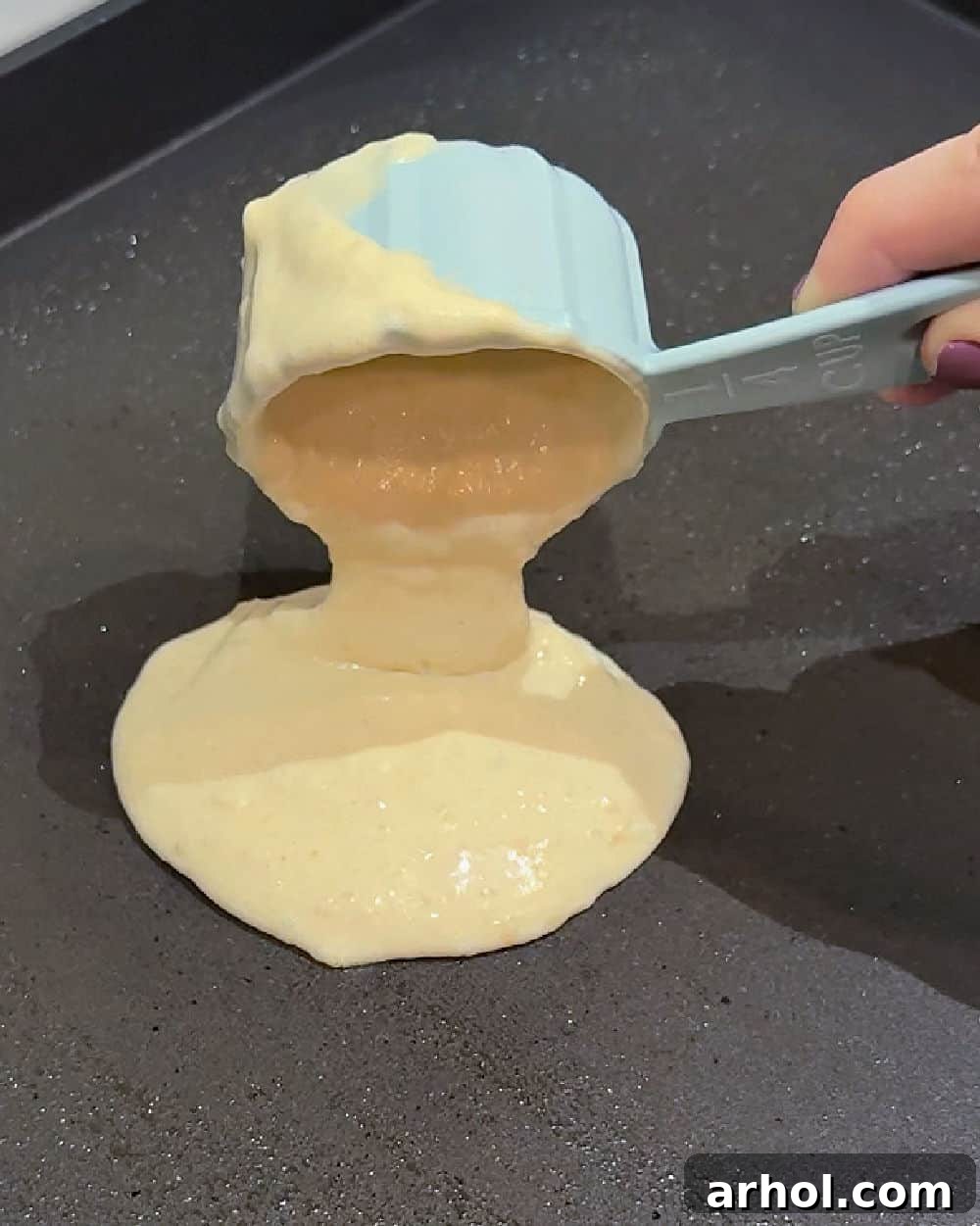 Pouring sourdough pancake batter from a measuring cup onto a hot griddle, forming a perfect round pancake.