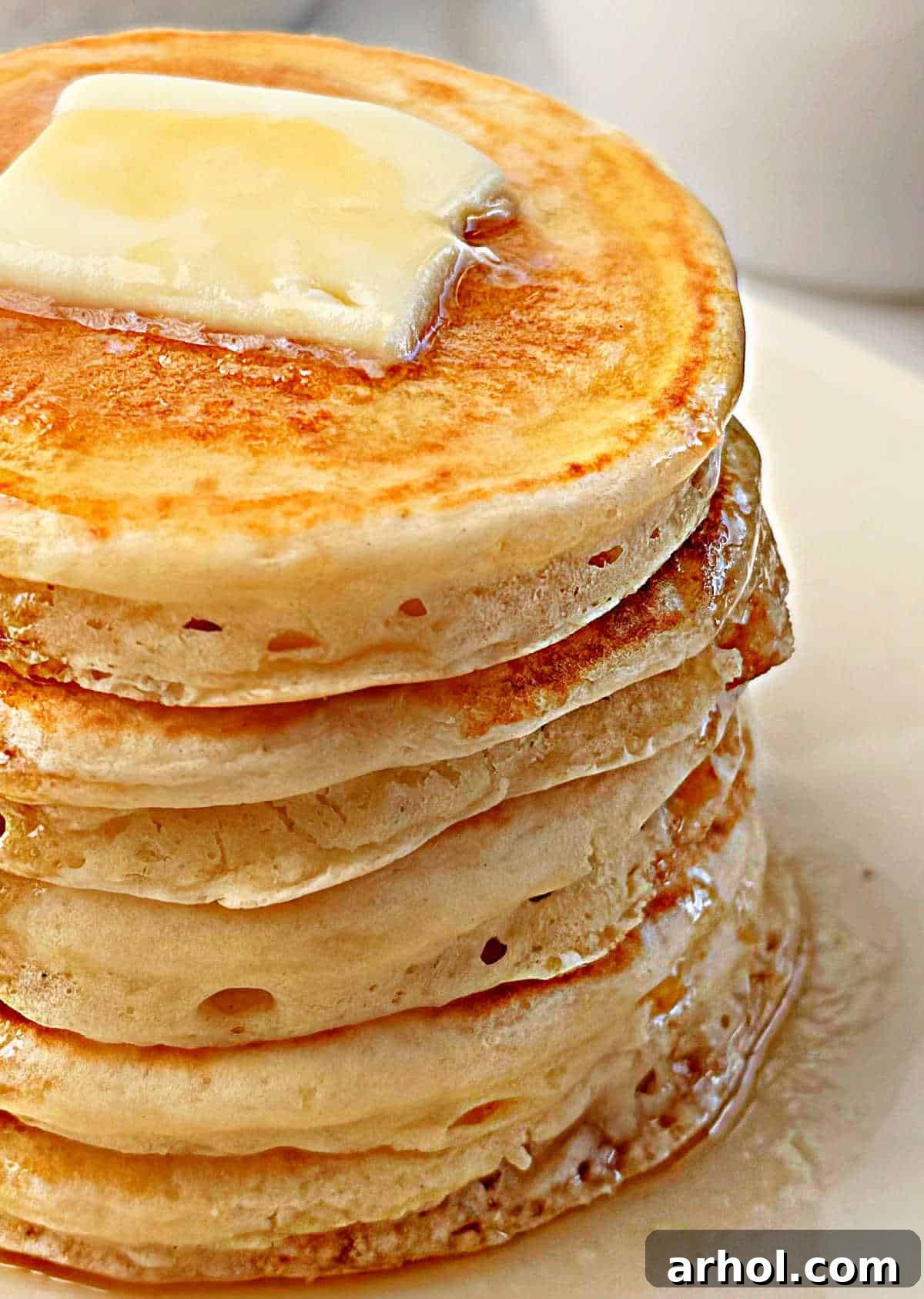 A towering stack of thick and fluffy sourdough pancakes, generously topped with melted butter and drizzled with maple syrup, ready to be enjoyed.