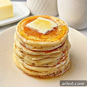 Fluffy sourdough pancakes topped with butter and maple syrup, presented on a rustic plate.