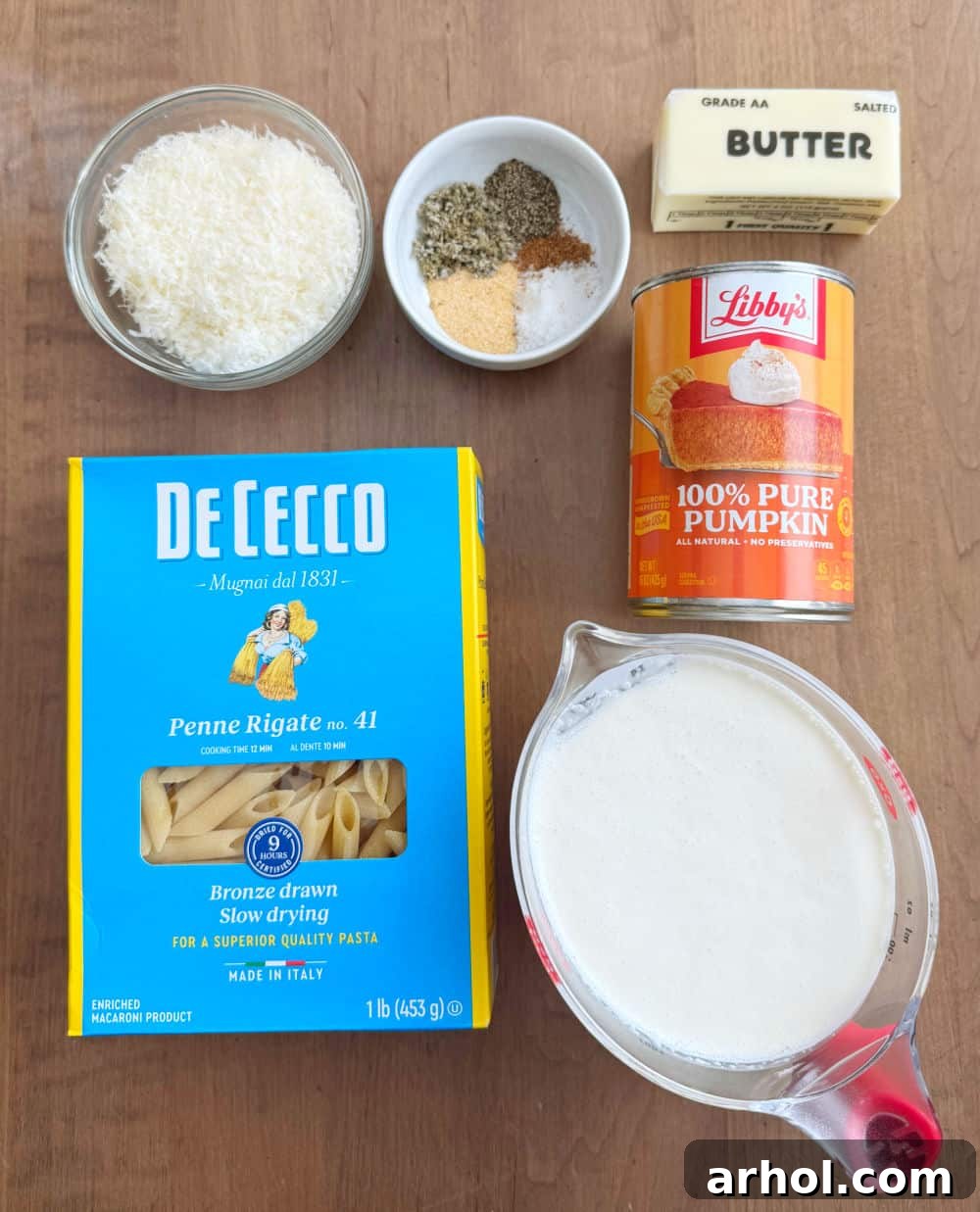 Effortless Pumpkin Pasta Perfection 4 Arrangement of key ingredients for pumpkin pasta sauce: a can of Libby's pumpkin puree, a carton of heavy cream, uncooked penne pasta, butter, various seasonings, and a block of Parmesan cheese.