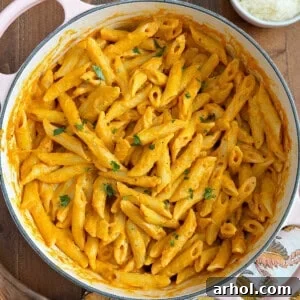Penne pasta with pumpkin pasta sauce, garnished with parsley, served in a Dutch oven, inviting to a delicious fall meal.