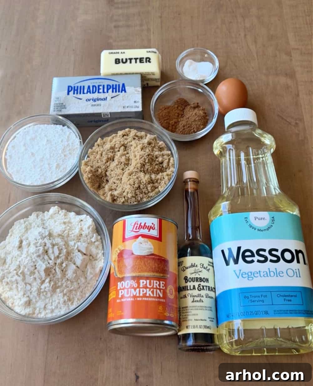 A flat lay photograph showcasing all the key ingredients for pumpkin whoopie pies: pumpkin puree, all-purpose flour, both brown and granulated sugars, butter, vegetable oil, an egg, vanilla extract, and a block of cream cheese.