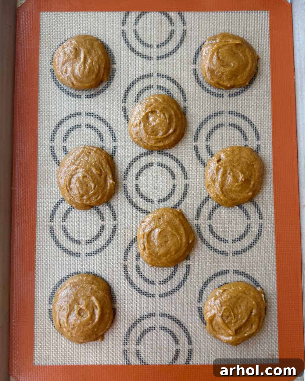 Pumpkin cookie rounds baking evenly spaced on a baking sheet lined with parchment paper, just starting to puff up.