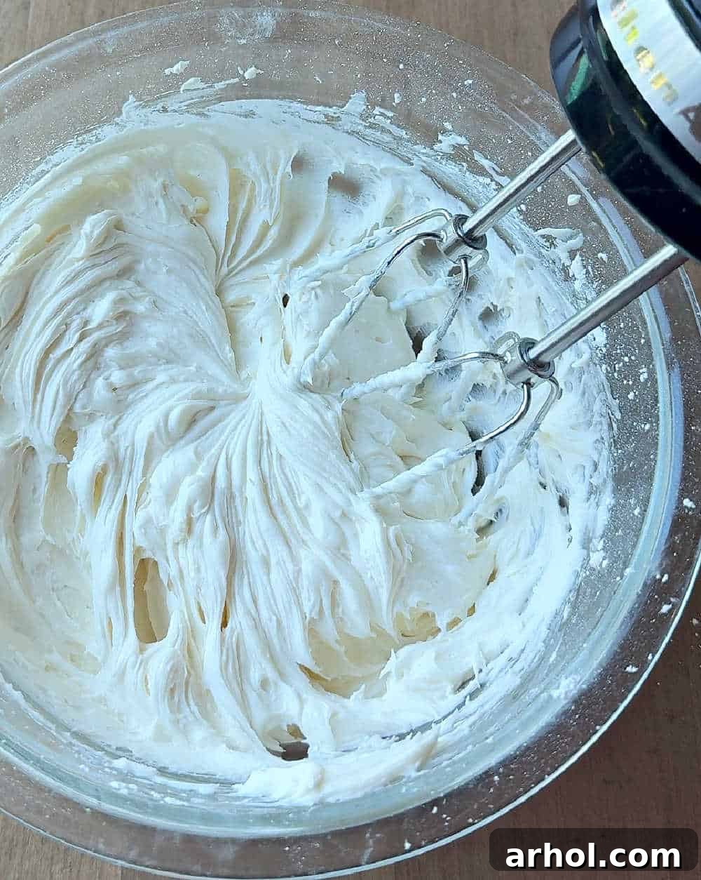 A bowl of creamy white frosting being mixed with a hand mixer, demonstrating the process of making the cream cheese filling.