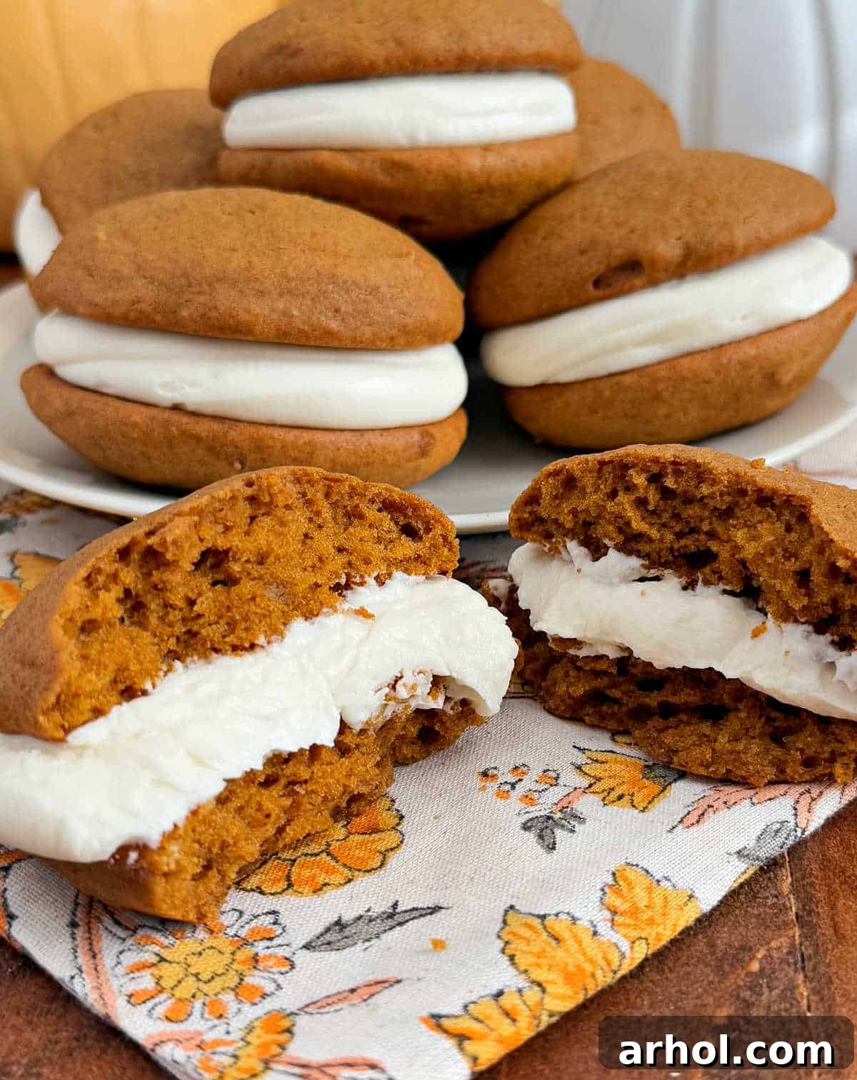 A delicious pumpkin whoopie pie on a plate, with another one sliced open in the foreground to show the creamy filling, all resting on a wooden table.