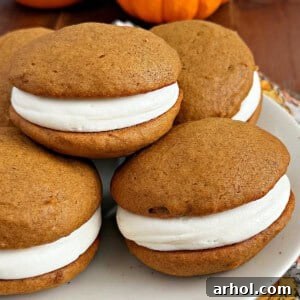 Close-up of a stack of pumpkin whoopie pies with visible cream cheese filling, garnished with a dusting of powdered sugar.