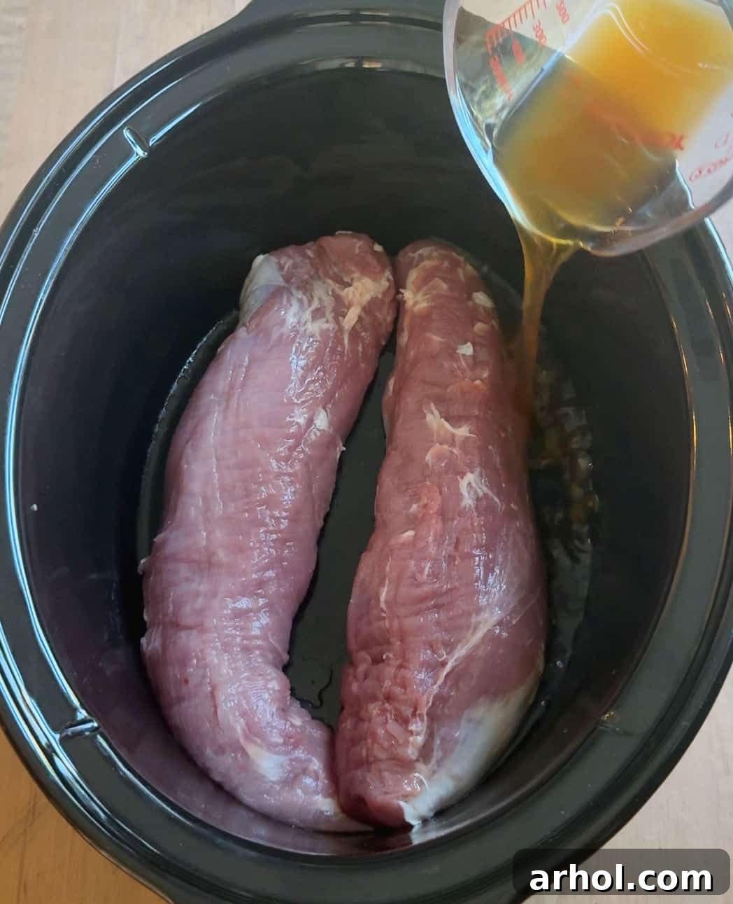 pouring broth over tenderloin in slow cooker.