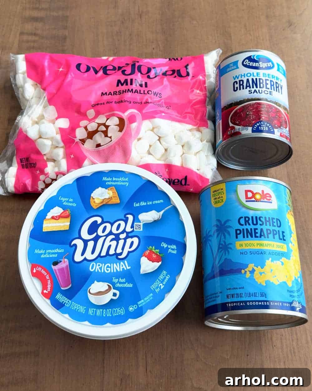 The four main ingredients laid out: a tub of Cool Whip, a can of crushed pineapple, a can of whole berry cranberry sauce, and a bag of mini marshmallows, ready for mixing.