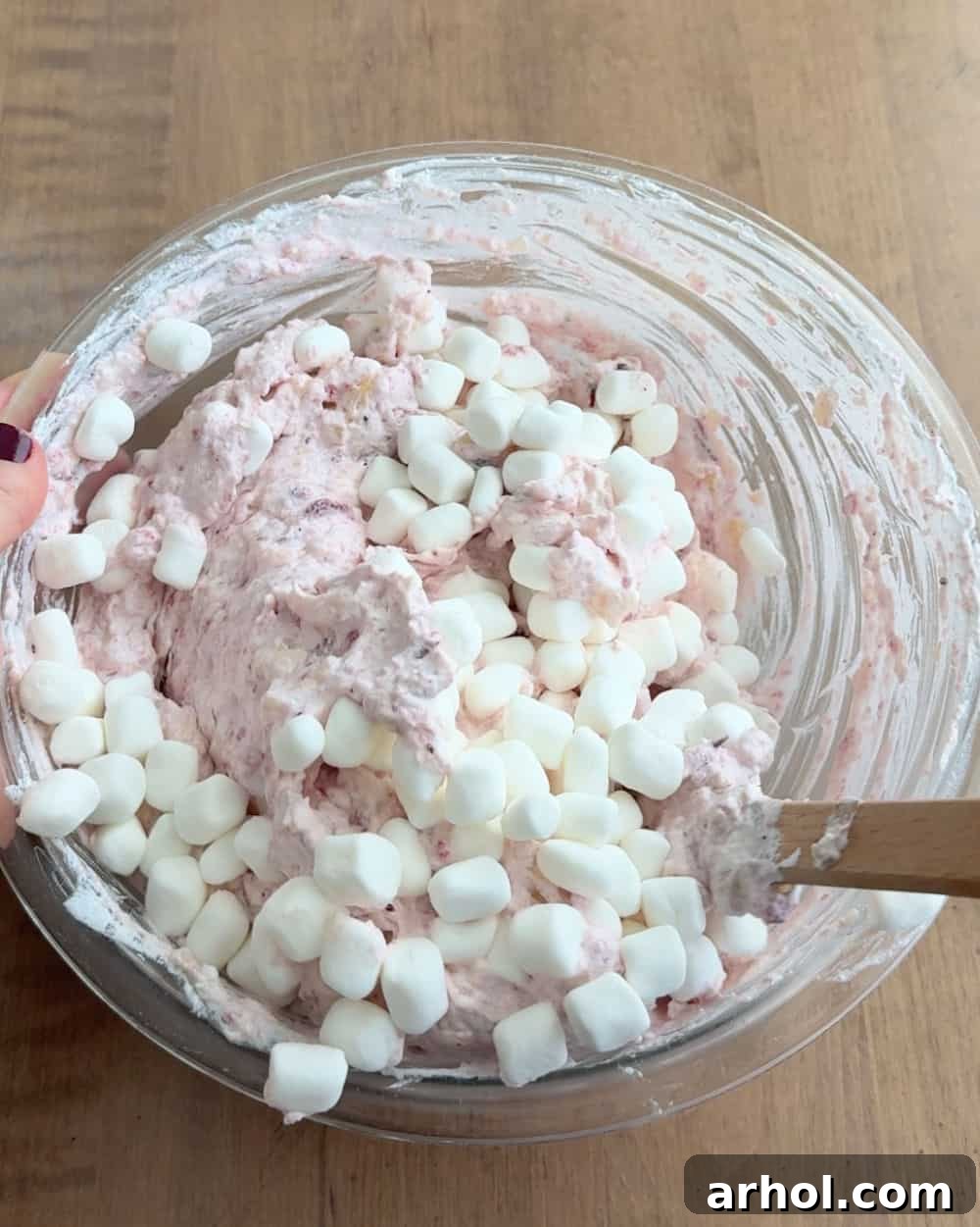 Stirring in the mini marshmallows as the final ingredient, ensuring they are evenly incorporated throughout the airy cranberry fluff.