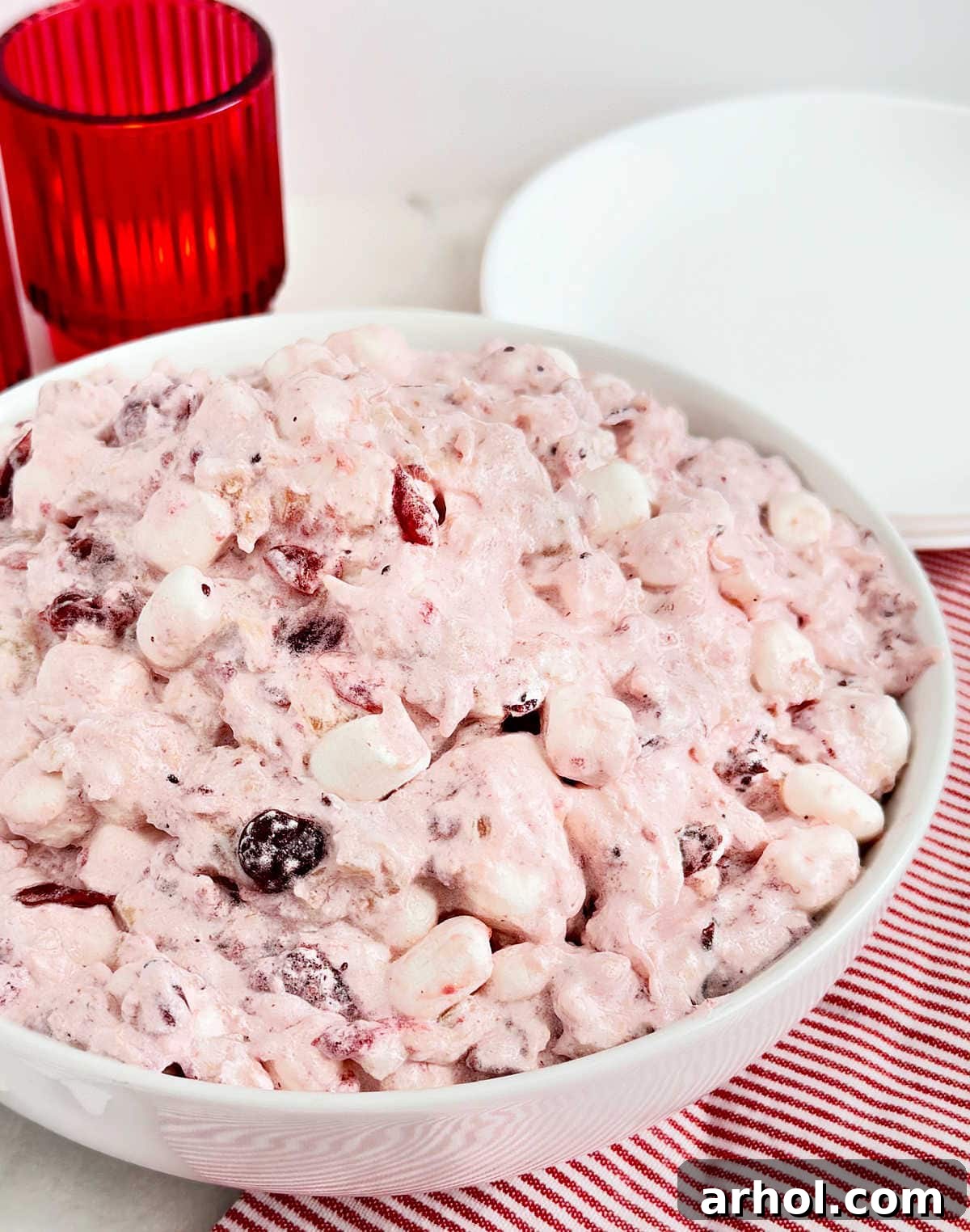 A large glass bowl overflowing with beautifully prepared Cranberry Fluff salad, ready for serving at a festive holiday meal, with cranberries scattered around.
