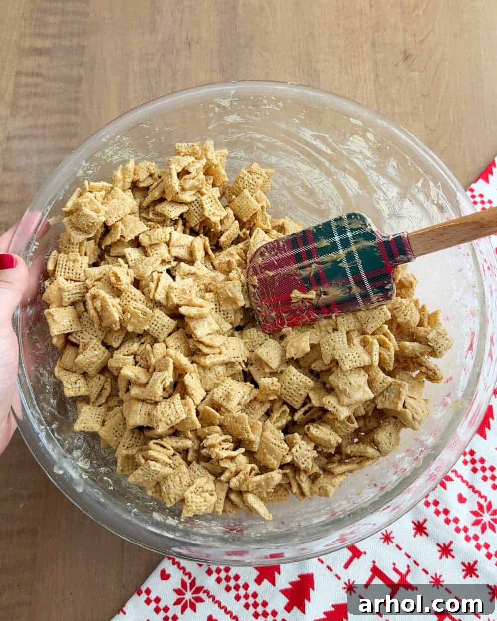 A spatula gently stirring Rice Chex cereal into the melted chocolate and peanut butter mixture, ensuring even coating for the peppermint muddy buddies.