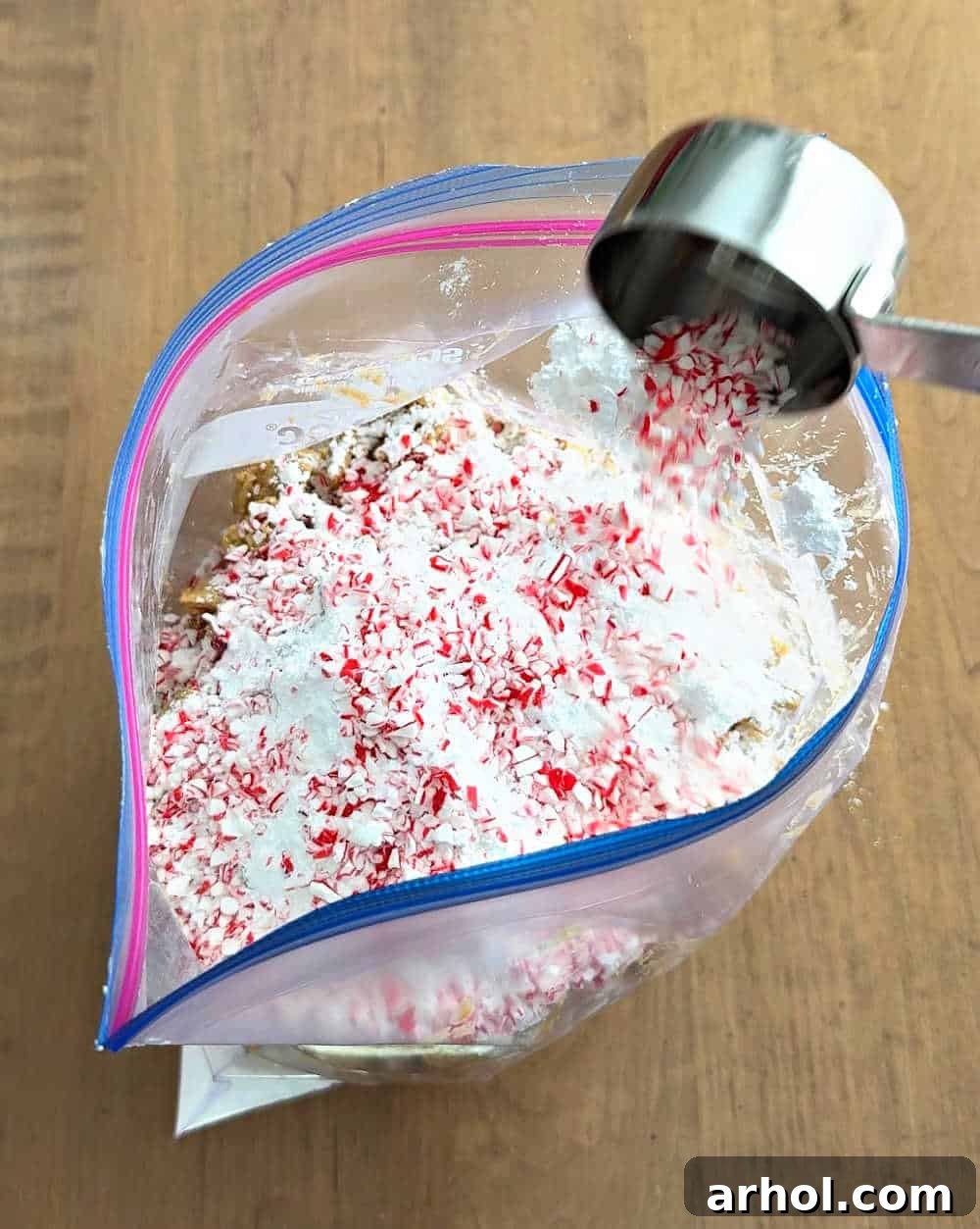 Powdered sugar and crushed candy canes being added to a large freezer bag containing chocolate-coated cereal, preparing for the final shake.