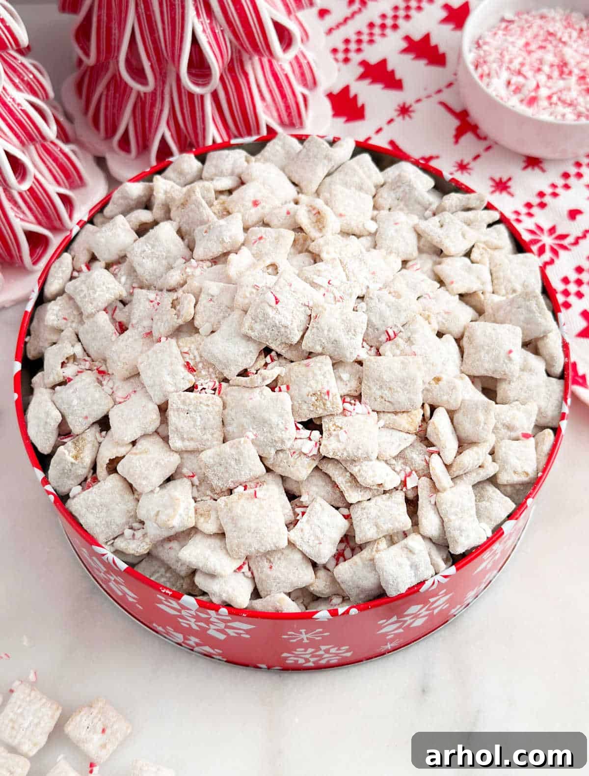 Festive peppermint puppy chow artfully arranged in a vibrant red holiday tin, making it a perfect gift or party snack.