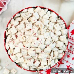 A close-up of festive peppermint puppy chow in a small bowl, adorned with extra crushed candy canes, showcasing its tempting texture.