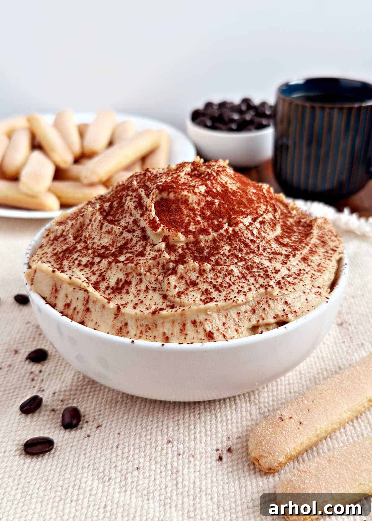 Spoonable Tiramisu Dream 2 A beautiful bowl of creamy tiramisu dip, generously dusted with cocoa powder, surrounded by crisp ladyfingers ready for dipping.