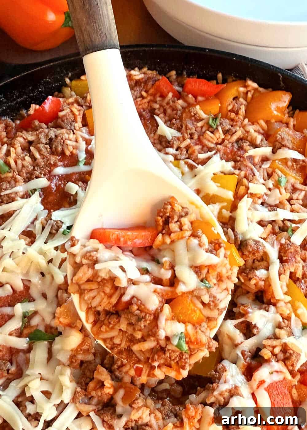 A serving spoon with unstuffed peppers and melted cheese, lifted from a skillet, showcasing the rich, savory texture.