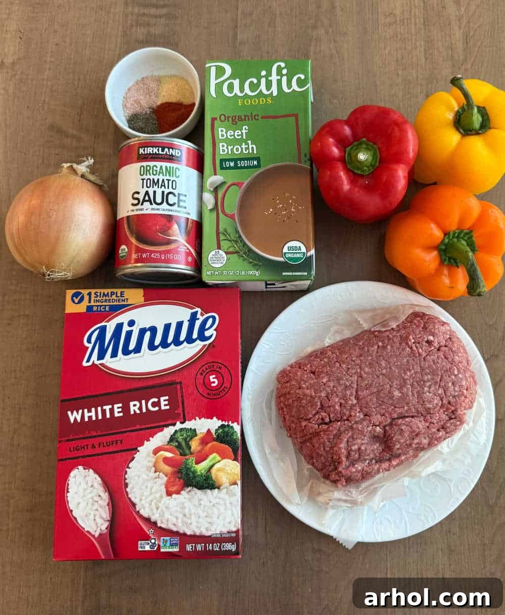 Fresh ingredients laid out for unstuffed peppers: rice, lean ground beef, diced onion, tomato sauce, assorted spices, rich beef broth, and a vibrant trio of red, orange, and yellow bell peppers.