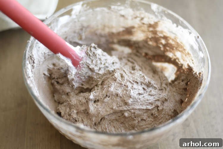 Mixing thawed Cool Whip and chocolate cake mix in a large glass bowl to form a sticky dough.