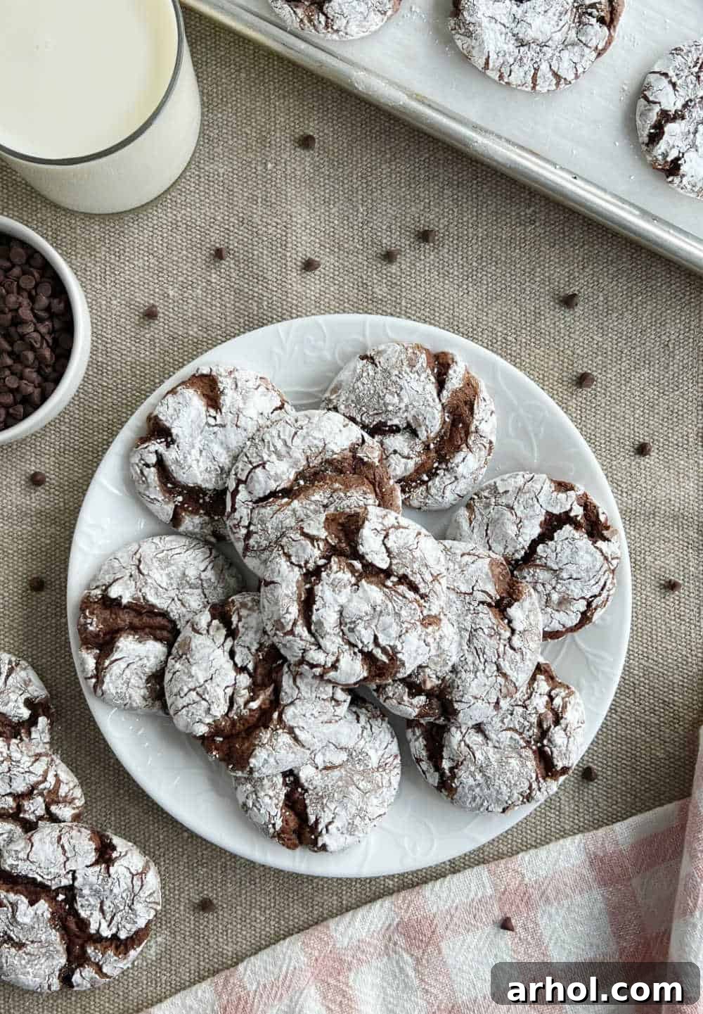 A beautiful plate of chocolate cake mix crinkle cookies, dusted with powdered sugar, sitting on a table.