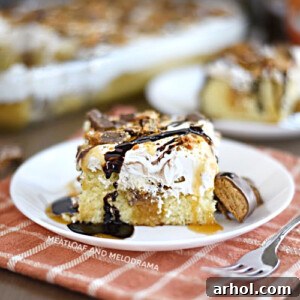 A delicious slice of Butterfinger poke cake with creamy Cool Whip frosting on a white plate, ready to be served and enjoyed.