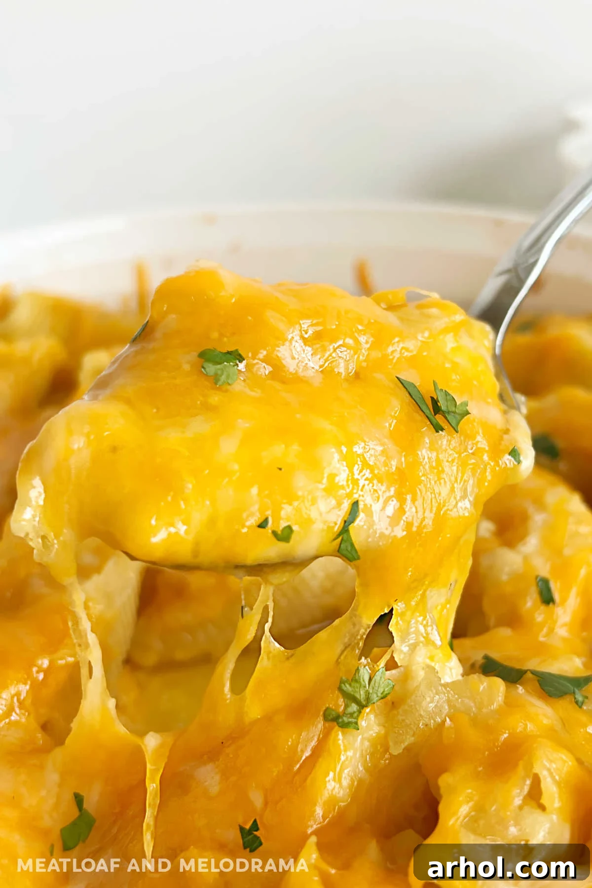 Serving spoon lifting pierogi stuffed shell topped with melted cheddar cheese and fresh parsley from a casserole dish