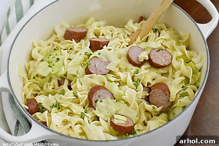A hearty serving of Haluski and Kielbasa in a white Dutch oven, featuring golden-fried cabbage, tender egg noodles, and sliced smoked sausage, a classic Pittsburgh comfort food.