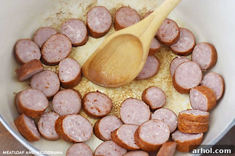 Sliced kielbasa browning in a large Dutch oven with onions, preparing for a delicious Haluski dish.