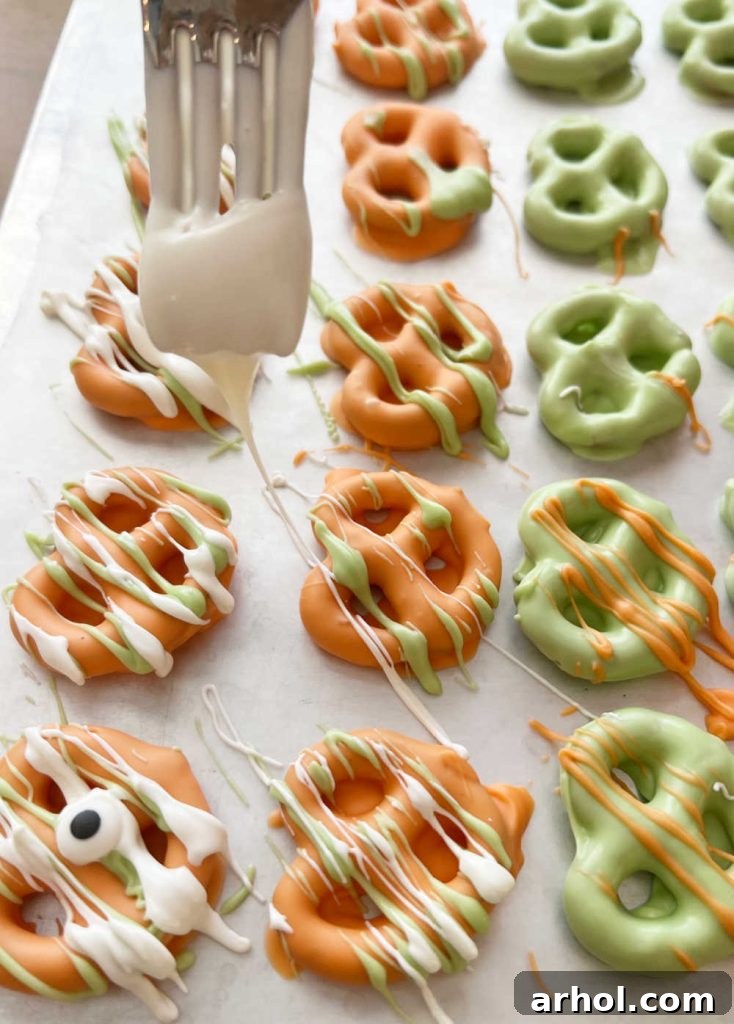 A fork is used to artfully drizzle contrasting melted candy coating over mini pretzels, adding an extra layer of color and design.
