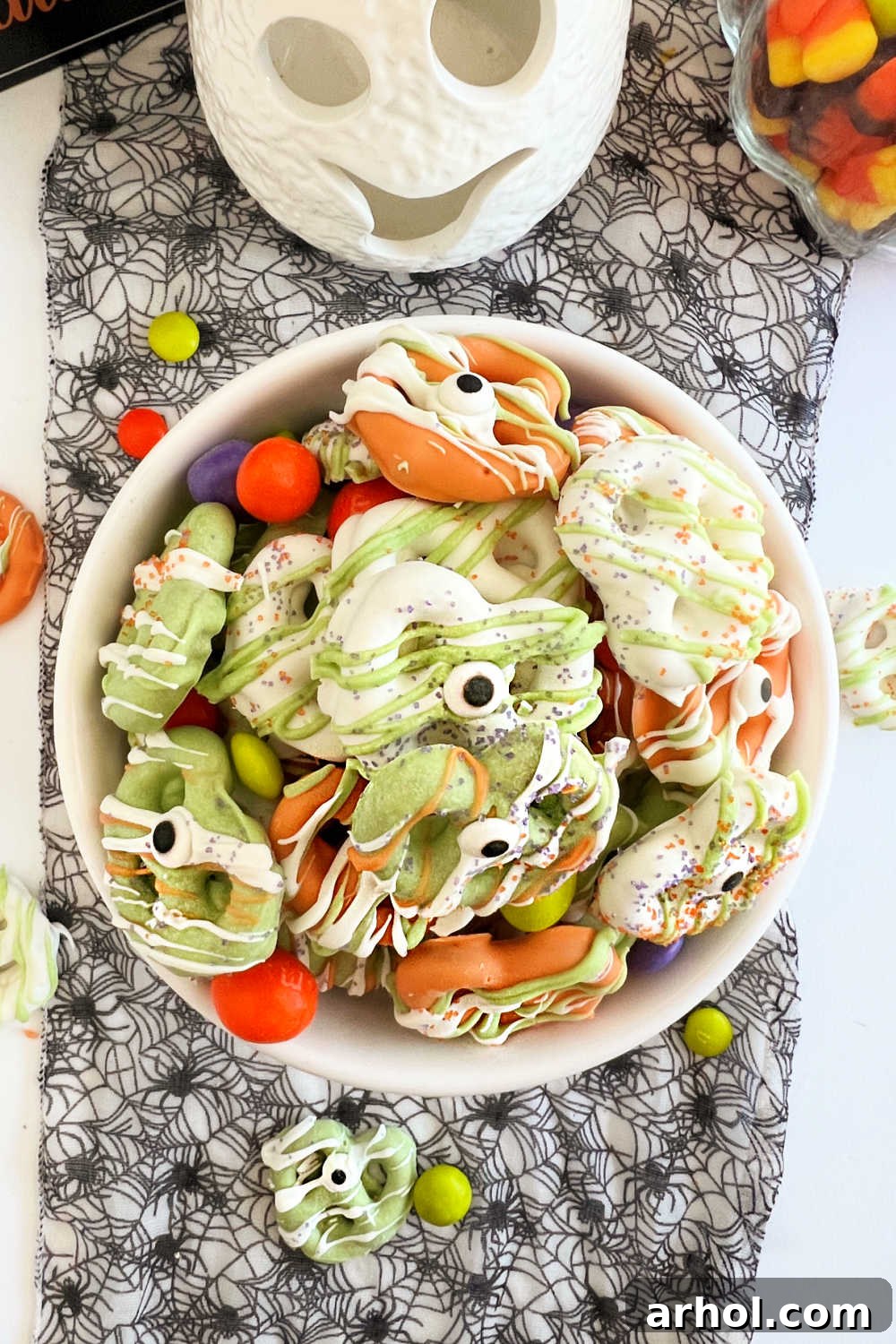 A vibrant bowl overflowing with green, white, and orange Halloween pretzels, each with an adorable candy eye, ready to be devoured as a spooky treat.