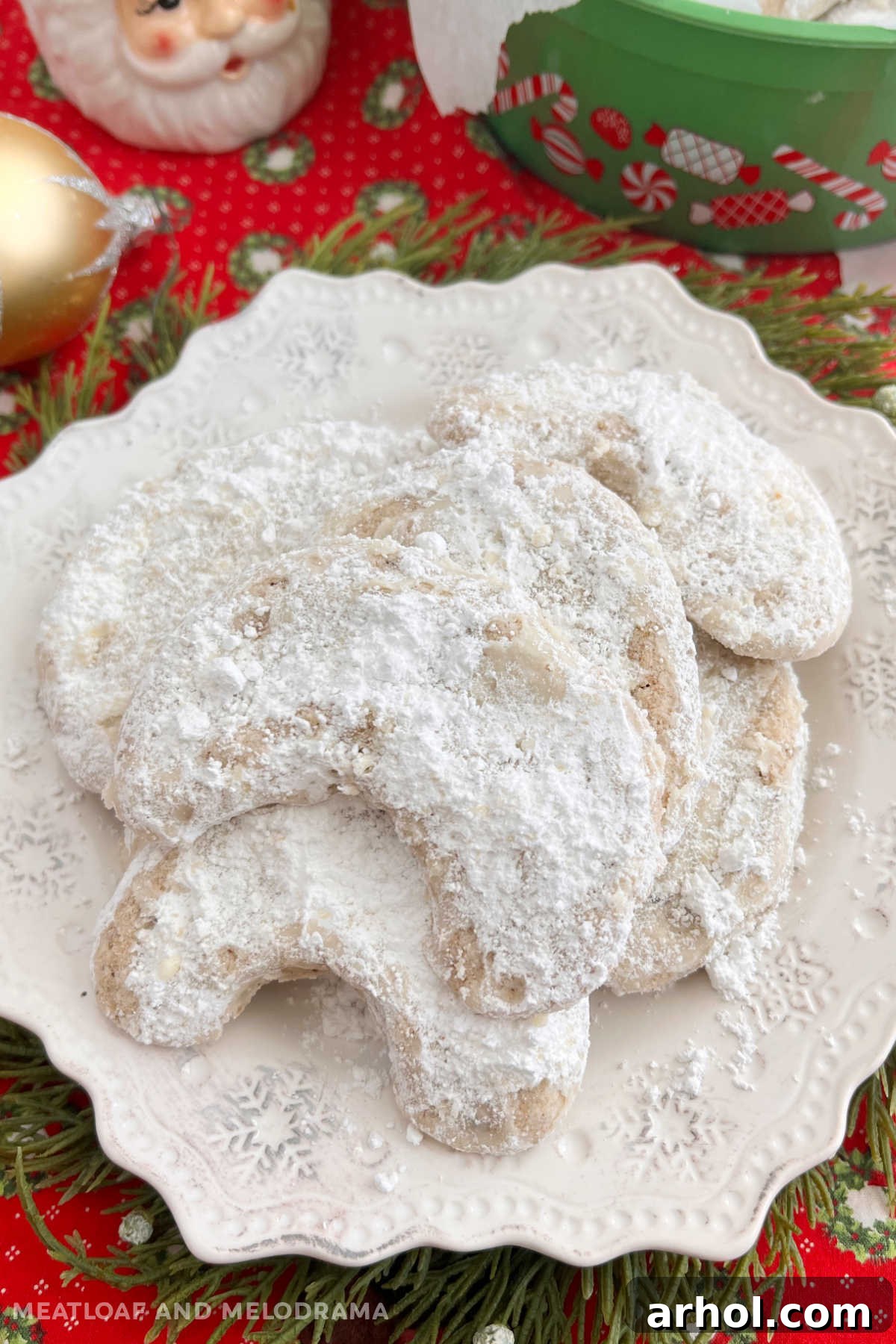 Plate of walnut crescent cookies in powdered sugar on a festive Christmas table, inviting hungry hands to grab one of these delicate treats.