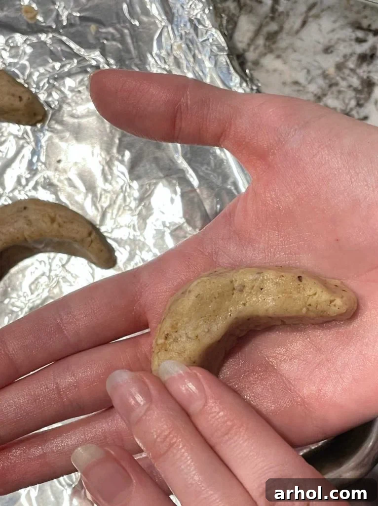 Hands shaping cookie dough into a crescent form, demonstrating the delicate process for these holiday cookies.