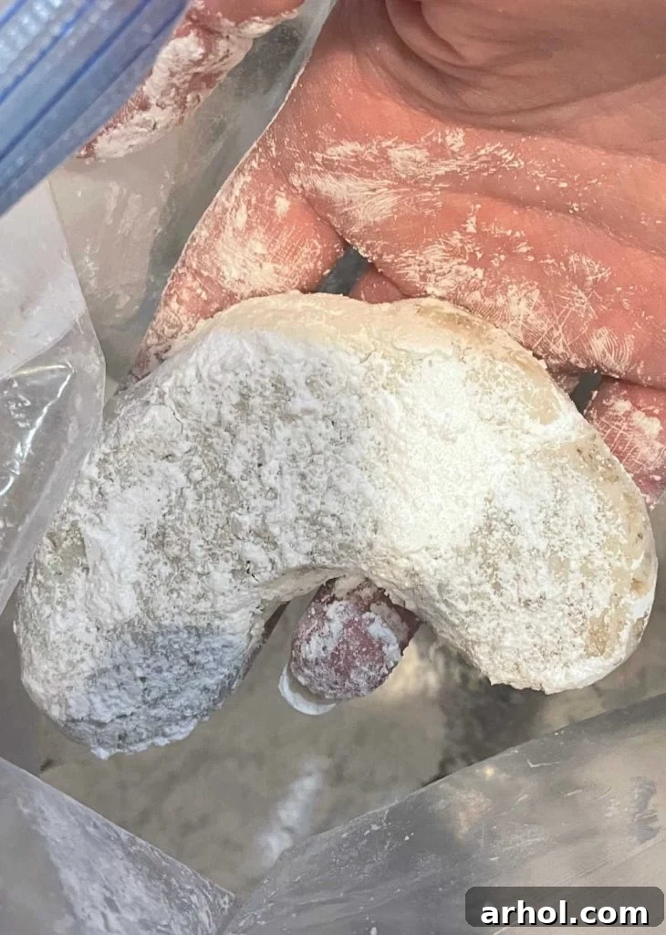 Walnut crescent cookie being dusted in powdered sugar, highlighting its classic holiday appearance.