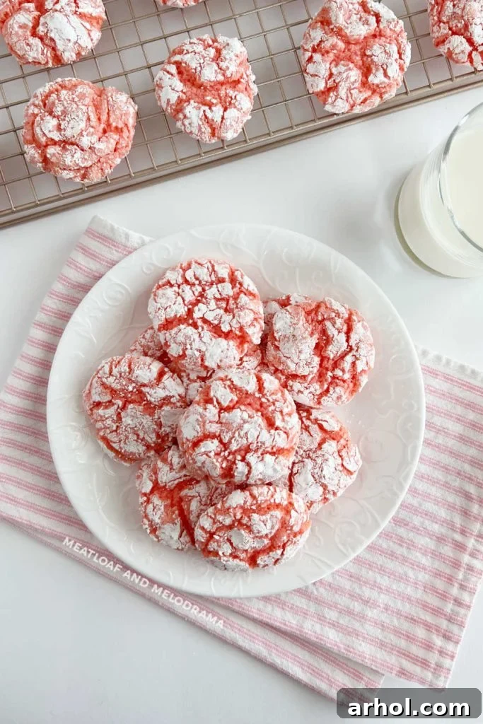 A beautiful plate of soft, chewy strawberry crinkle cookies, perfectly dusted with powdered sugar, sitting next to a glass of milk on a rustic wooden table. Ideal for Valentine's Day, Easter, or any spring celebration.