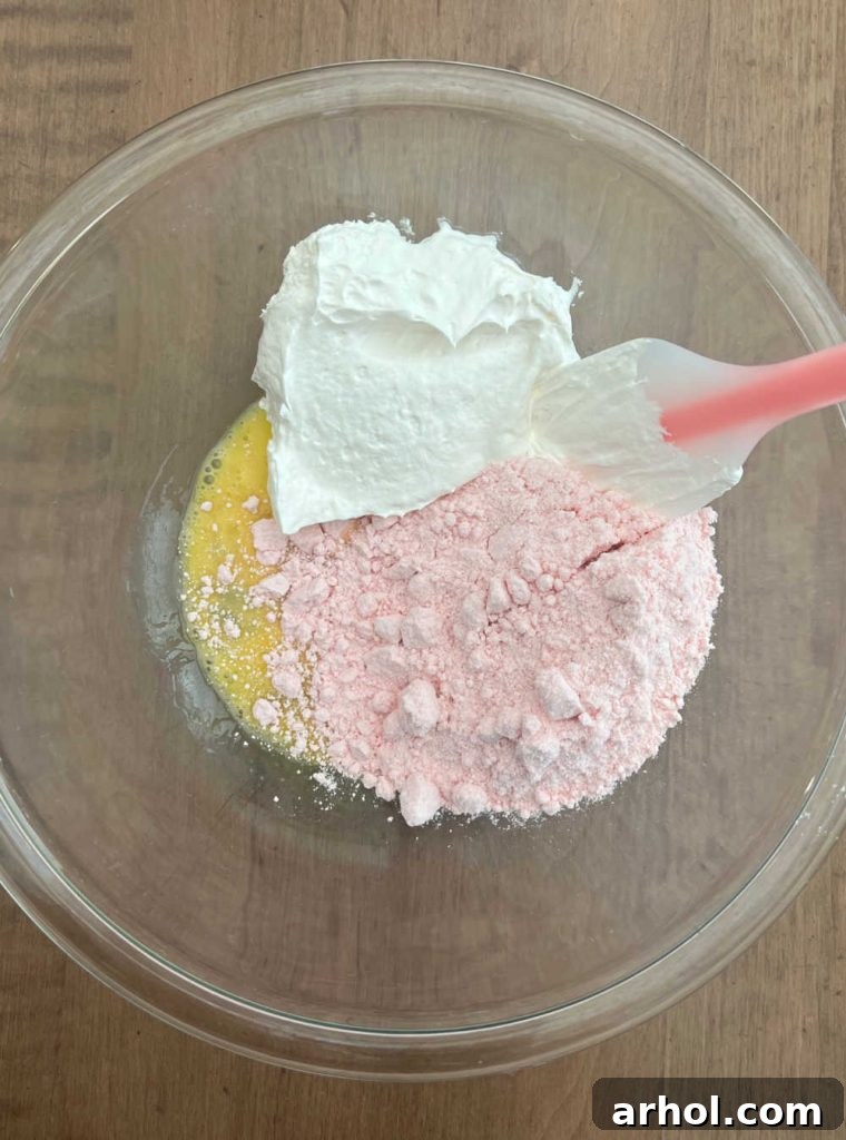 A mixing bowl containing strawberry cake mix, Cool Whip, and a single egg, ready to be combined into cookie dough.