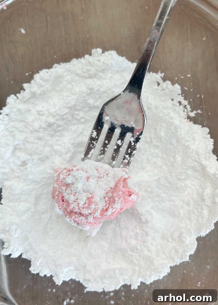 Strawberry cake mix cookie dough balls generously coated in powdered sugar, ready for baking to create their signature crinkles.