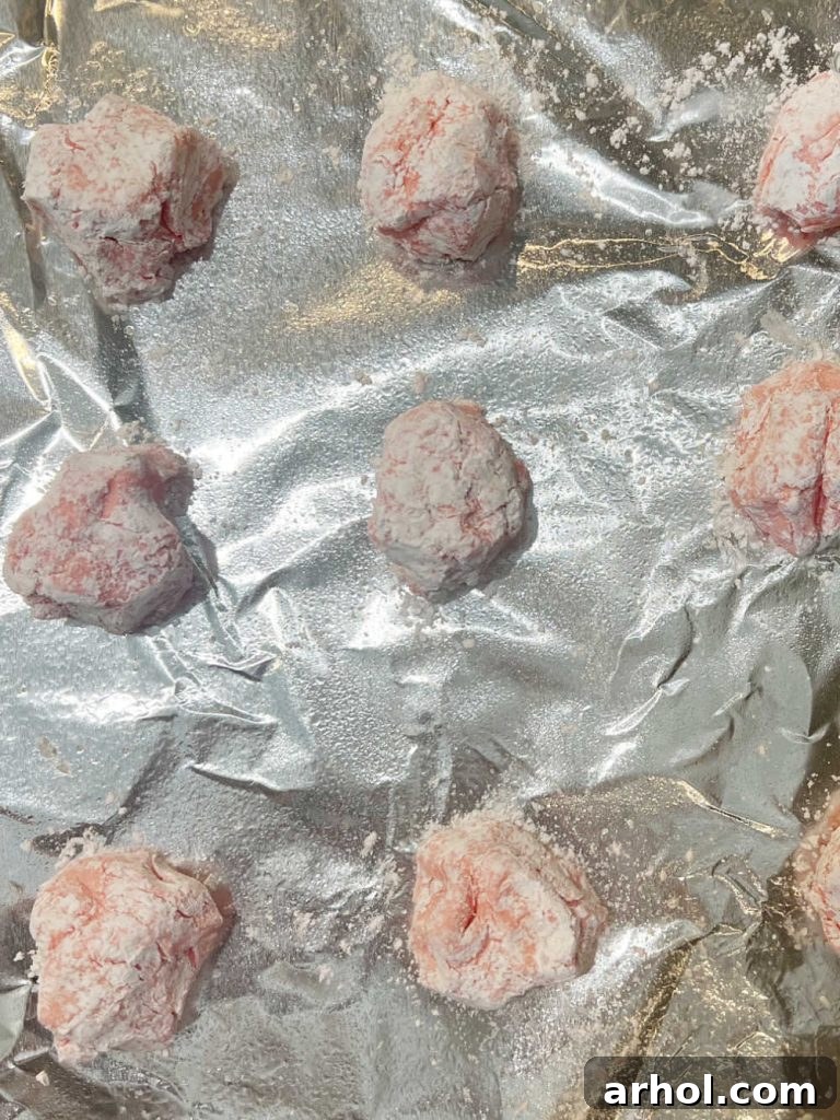 Unbaked strawberry cake mix cookies, rolled in powdered sugar, neatly arranged on a prepared cookie sheet, spaced out and ready to go into the oven.